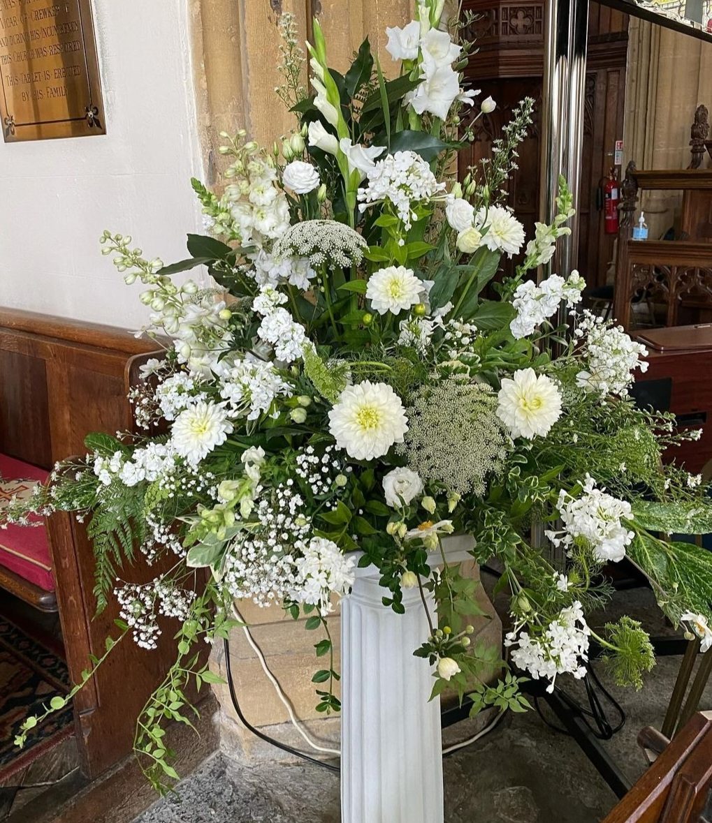 Tall white and green pedestal arrangement of roses, dahlias and gypsophila inside a church