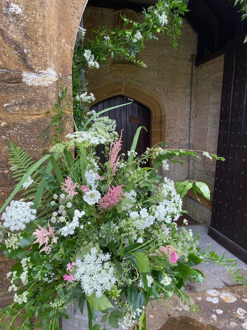 Large urn arrangement of white, pink and green flowers beside a stone church doorway