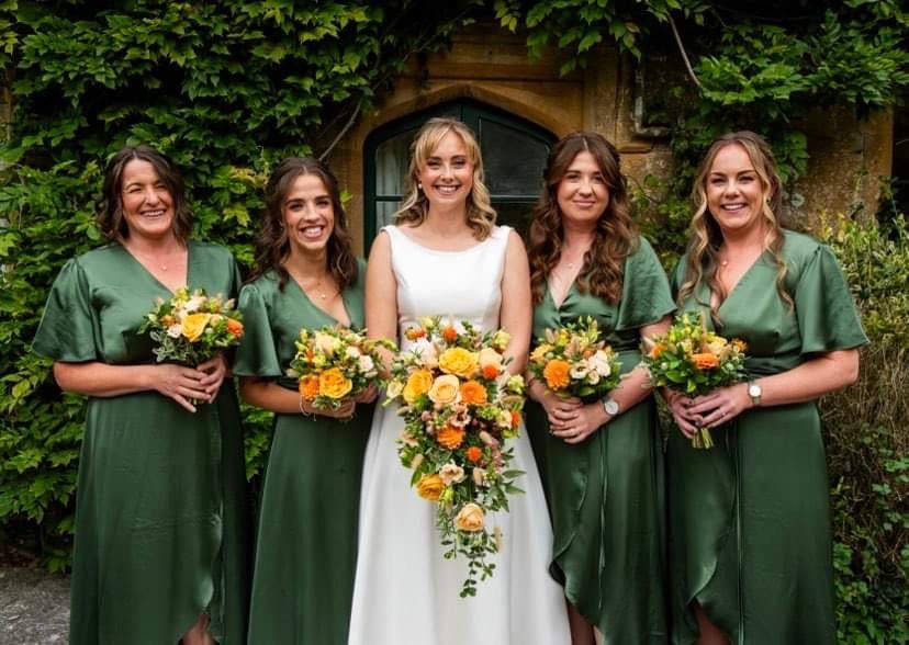 Bride and four bridesmaids in green holding orange and yellow bouquets, the bride with a trailing design